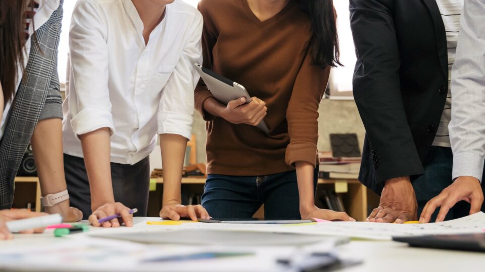 Close-up: people leaning on table while discussing ideas in workshop